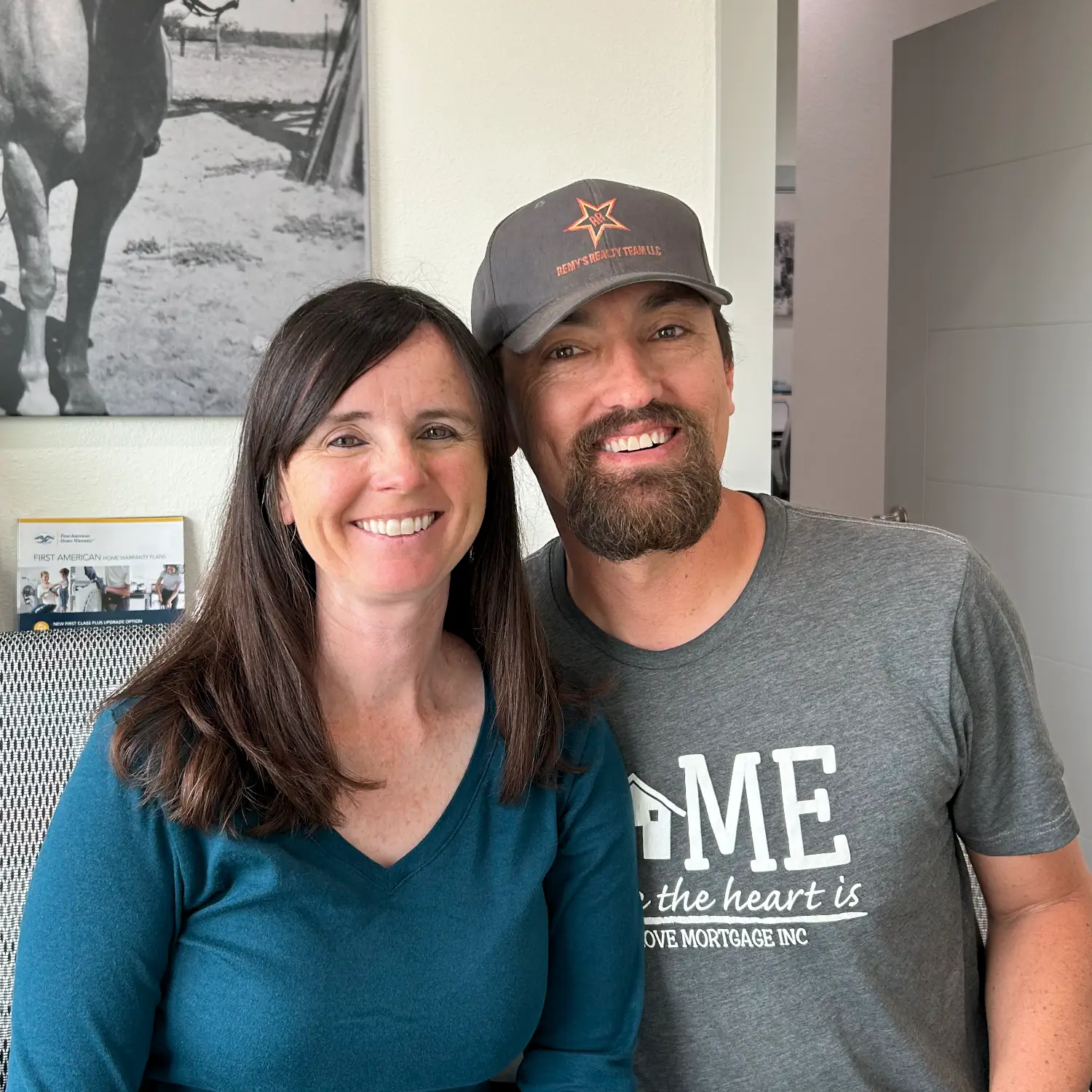 A smiling man wearing a Love Mortgage Inc. t-shirt and a Remy's Realty cap poses next to a woman in a blue shirt.