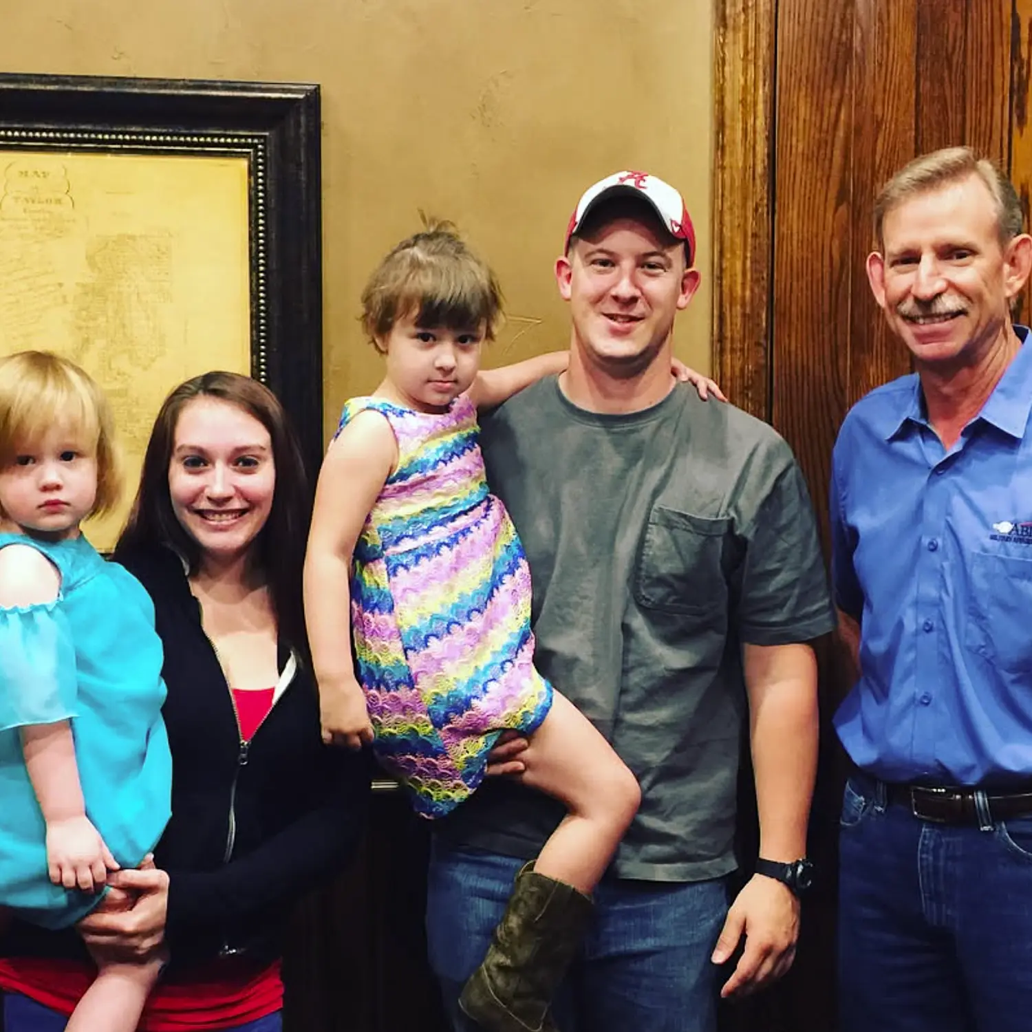A smiling young family of four poses happily with their mortgage broker in a blue shirt after closing on their new home.