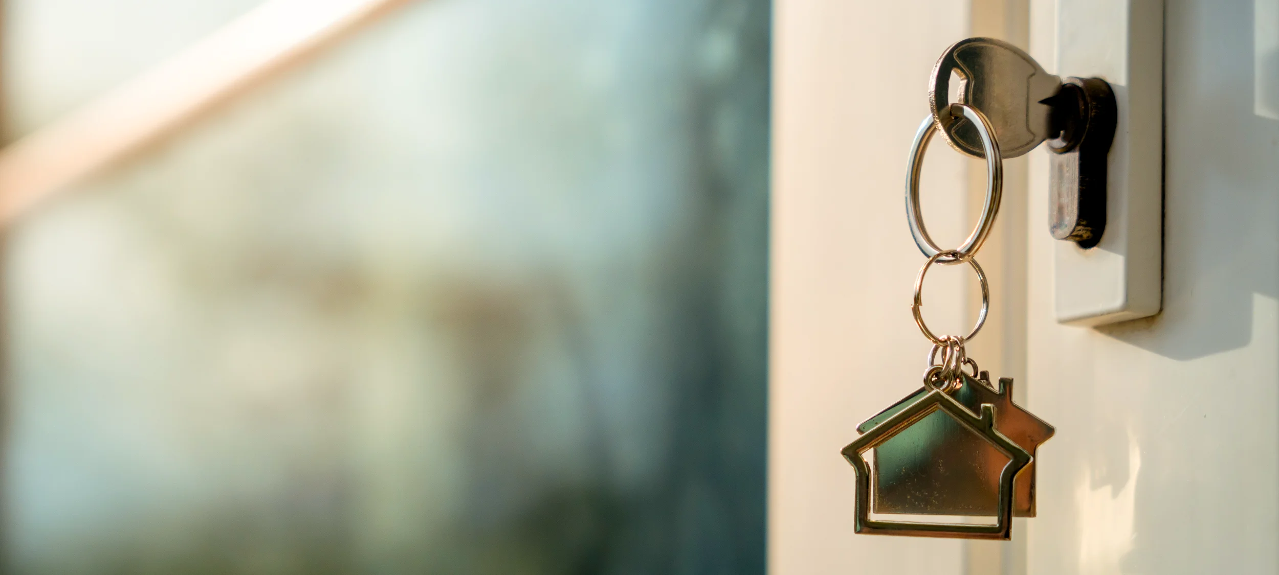 A key with two metallic, house-shaped keychains is inserted into the lock of a door, suggesting the moment of gaining entry to a new home.