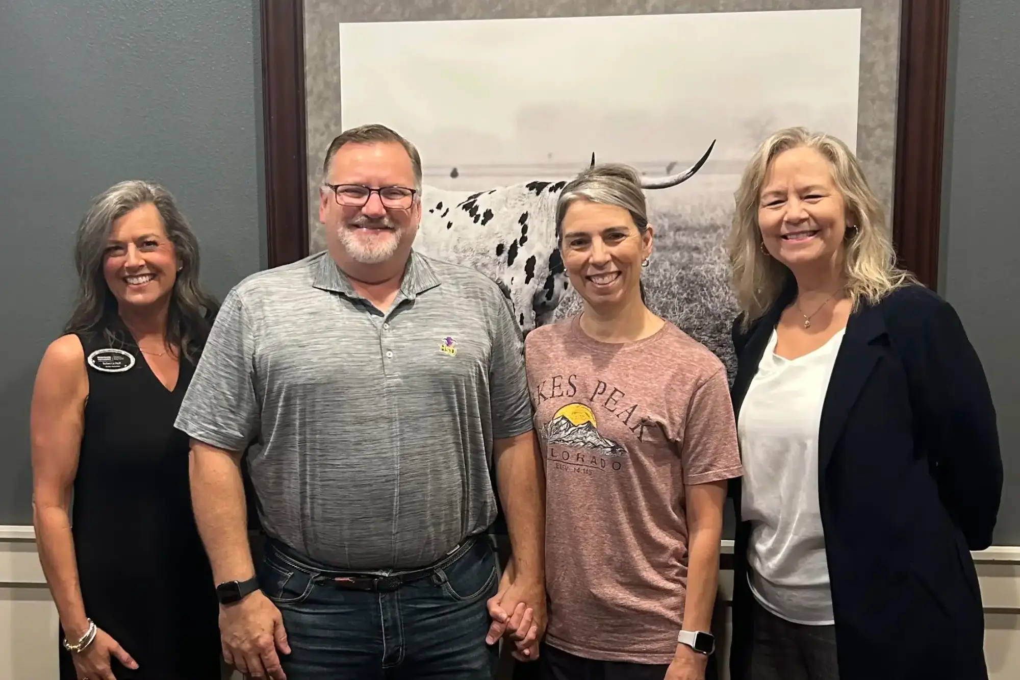Four smiling individuals, a couple and two professionals, stand together celebrating a house closing. The couple in the center holds hands warmly.