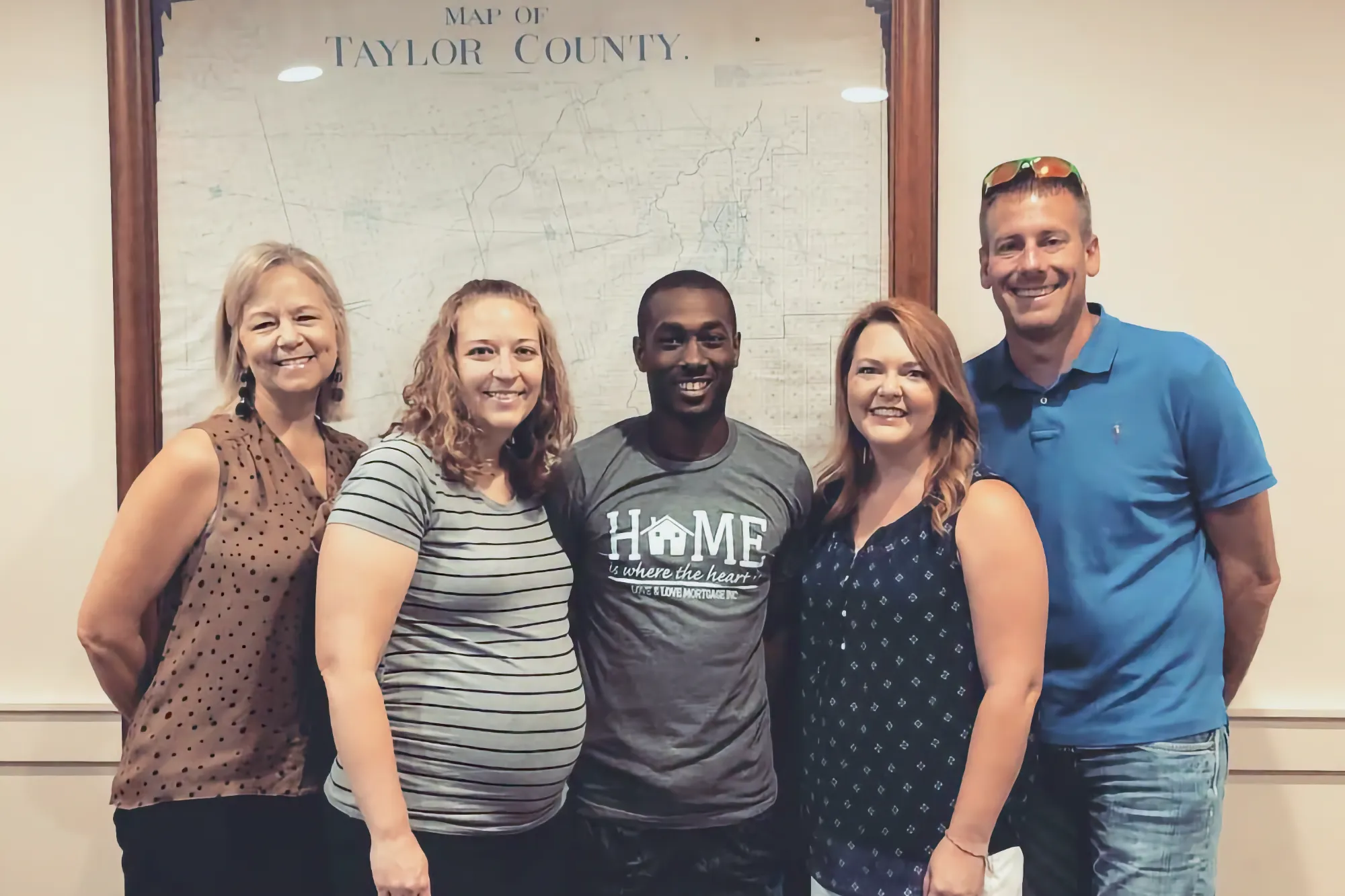 A group of five smiling peoples stand happily together, including a pregnant woman. They are celebrating a successful closing in an office setting.
