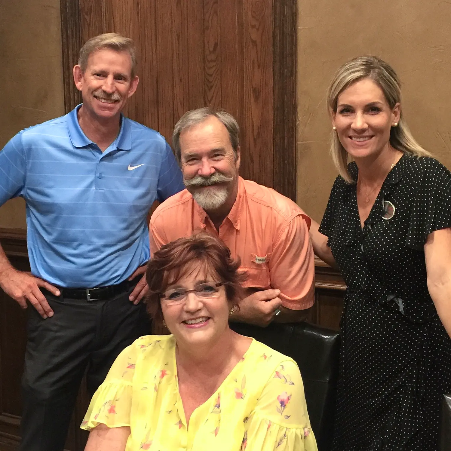 A realtor and three clients, including an older couple, smile happily together after a successful closing. They pose indoors against a wooden background.